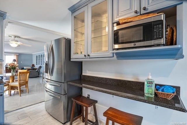 kitchen featuring gray cabinetry, ceiling fan, a kitchen breakfast bar, dark stone countertops, and appliances with stainless steel finishes