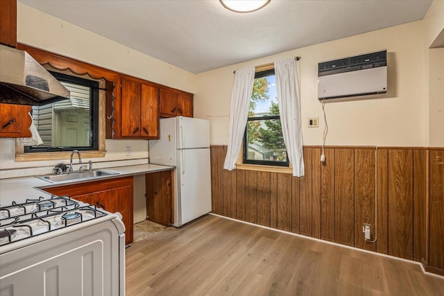 kitchen with sink, light hardwood / wood-style flooring, ventilation hood, wood walls, and white appliances