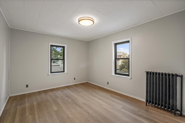 unfurnished room with radiator heating unit, light wood-type flooring, and a healthy amount of sunlight