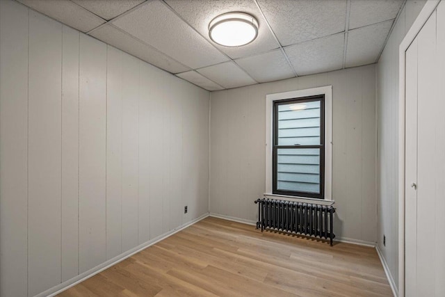 spare room with radiator heating unit, light wood-type flooring, wooden walls, and a paneled ceiling