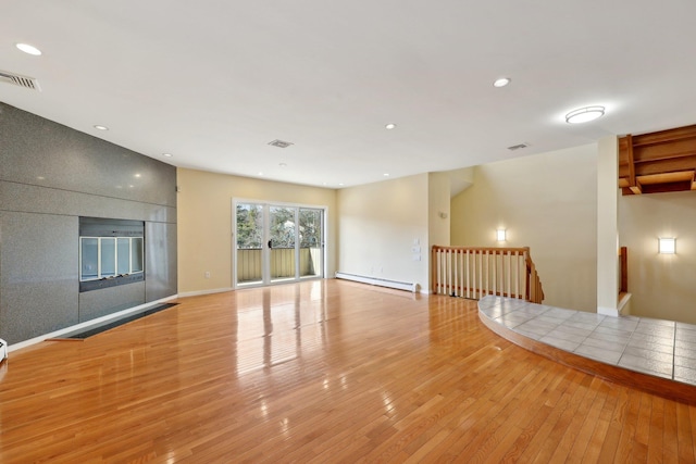 unfurnished living room with light hardwood / wood-style floors and a baseboard heating unit