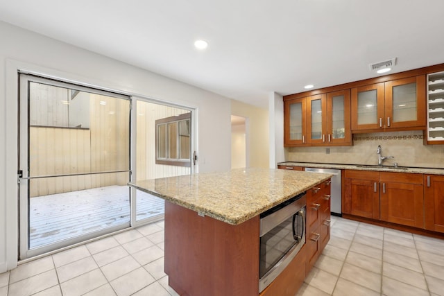 kitchen with a center island, sink, light stone countertops, light tile patterned flooring, and stainless steel appliances