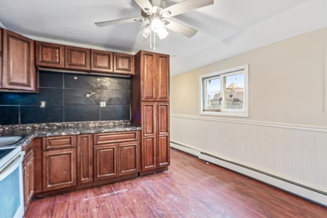 kitchen with ceiling fan, wood-type flooring, a baseboard radiator, dark stone countertops, and range