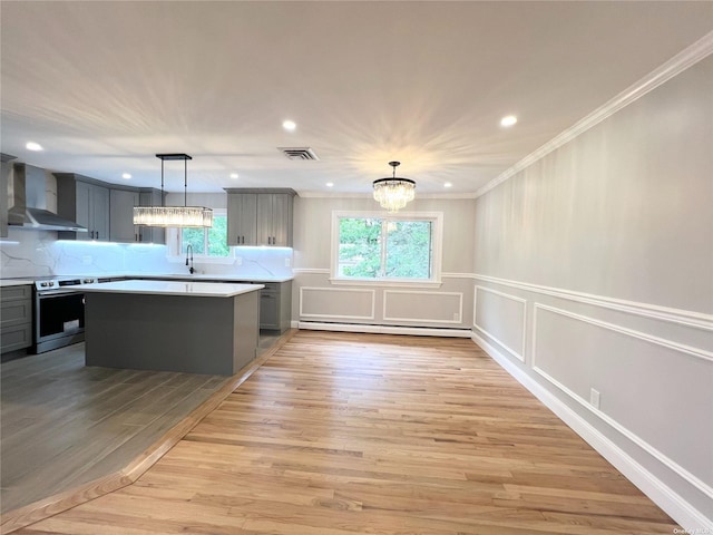 kitchen with stainless steel range with electric stovetop, wall chimney exhaust hood, decorative light fixtures, light hardwood / wood-style flooring, and a chandelier