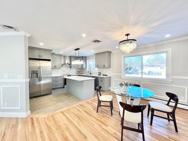 kitchen with wall chimney exhaust hood, light hardwood / wood-style floors, stainless steel appliances, decorative light fixtures, and gray cabinets