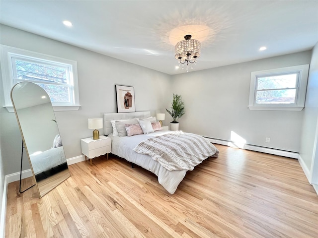 bedroom featuring baseboard heating, light hardwood / wood-style flooring, and an inviting chandelier