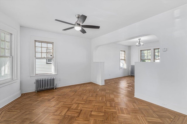 unfurnished room with radiator heating unit, parquet floors, and ceiling fan with notable chandelier