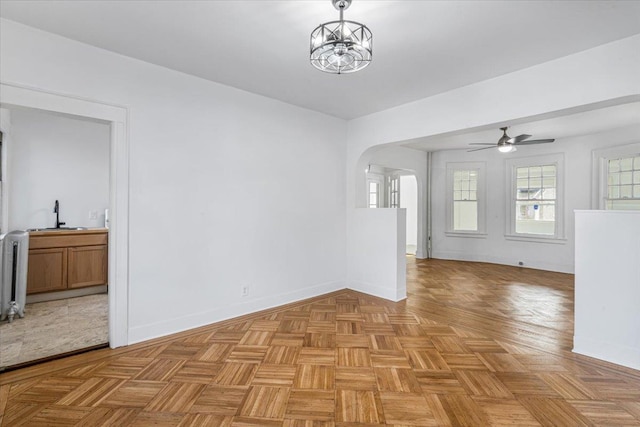 spare room featuring radiator heating unit, light parquet floors, ceiling fan with notable chandelier, and sink