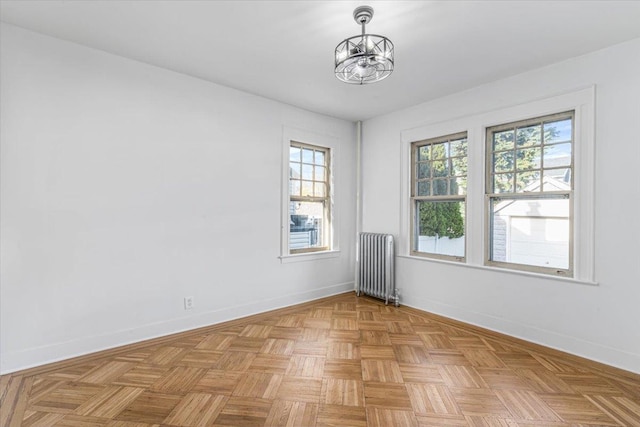 spare room featuring a wealth of natural light, radiator, and an inviting chandelier