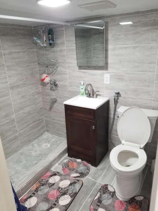 bathroom featuring vanity, tile patterned floors, toilet, tile walls, and a tile shower