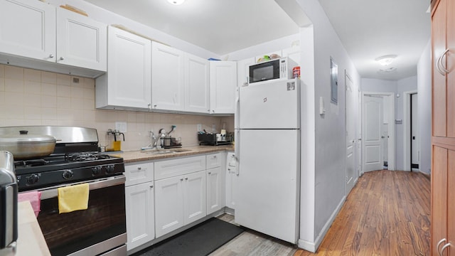 kitchen with sink, backsplash, white appliances, white cabinets, and light wood-type flooring