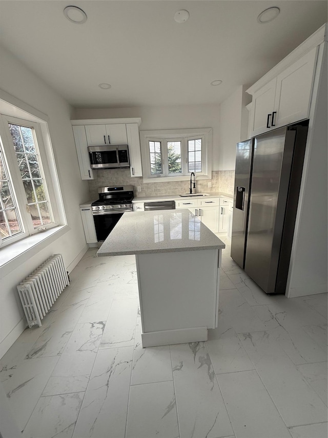 kitchen featuring radiator, a center island, white cabinets, and appliances with stainless steel finishes