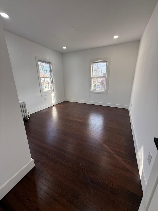 empty room featuring dark hardwood / wood-style flooring, radiator, and a wealth of natural light