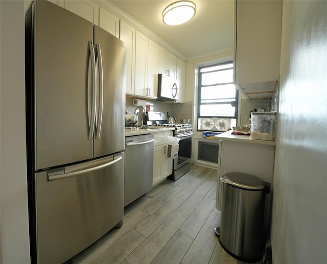 kitchen with white cabinetry, crown molding, light hardwood / wood-style floors, decorative backsplash, and appliances with stainless steel finishes