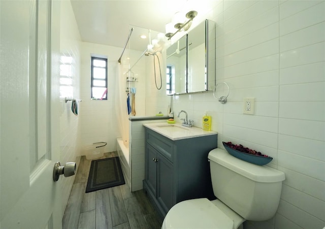 full bathroom featuring vanity, tiled shower / bath, tile walls, and toilet