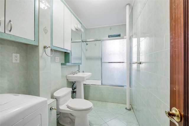 bathroom with shower / bath combination with glass door, tile patterned floors, toilet, tile walls, and washer / dryer