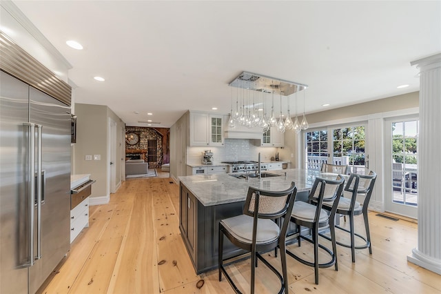 kitchen featuring white cabinetry, a large island, built in refrigerator, light stone countertops, and pendant lighting