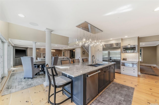 kitchen with decorative columns, an island with sink, a kitchen breakfast bar, built in appliances, and sink