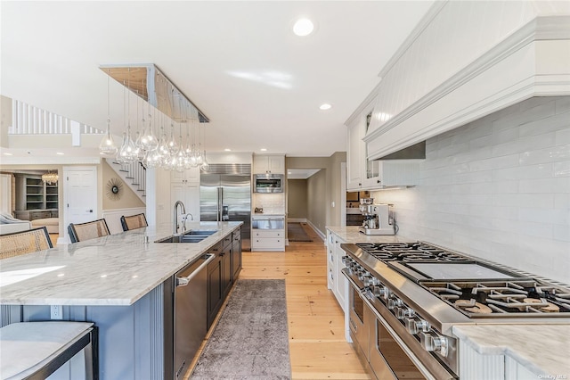 kitchen featuring a spacious island, pendant lighting, white cabinets, built in appliances, and sink