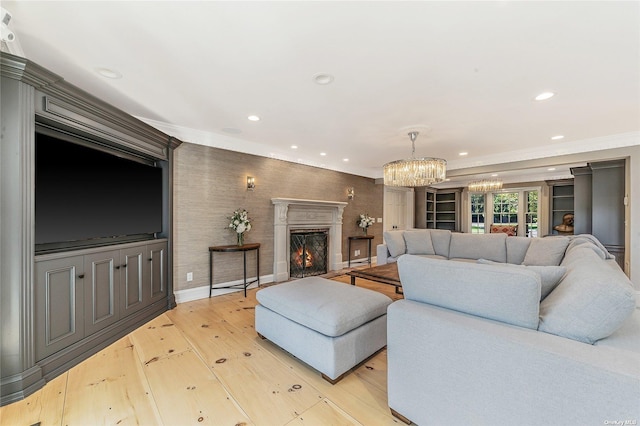 living room with light wood-type flooring, ornamental molding, a fireplace, and a notable chandelier