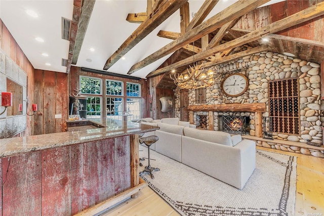 living room with light wood-type flooring, a chandelier, a stone fireplace, and lofted ceiling with beams