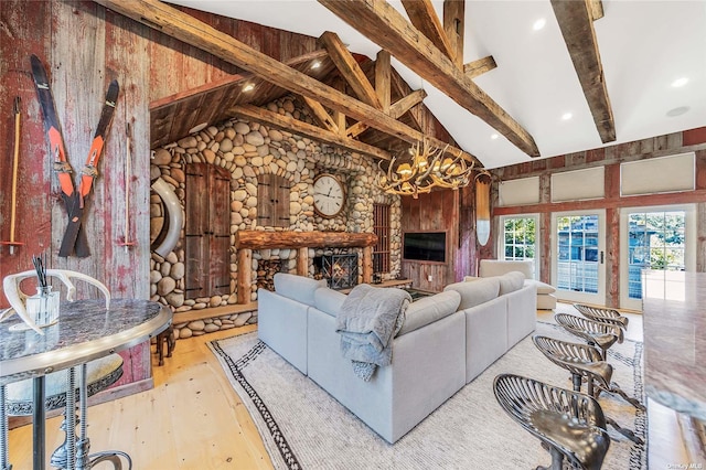 living room featuring a notable chandelier, beam ceiling, light wood-type flooring, a stone fireplace, and high vaulted ceiling