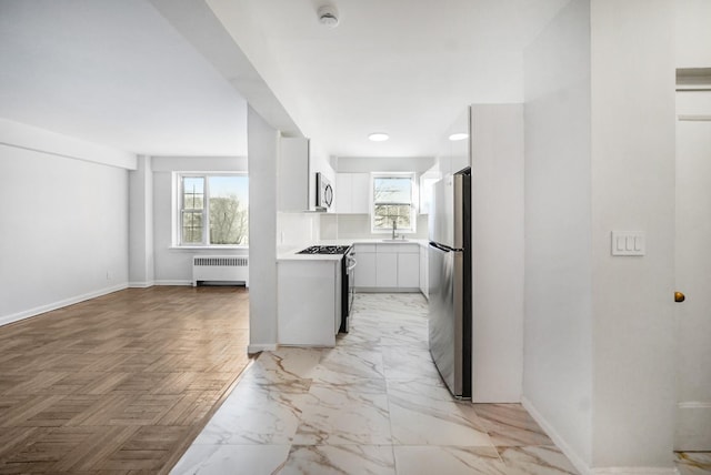 kitchen with sink, radiator heating unit, light parquet flooring, white cabinets, and appliances with stainless steel finishes