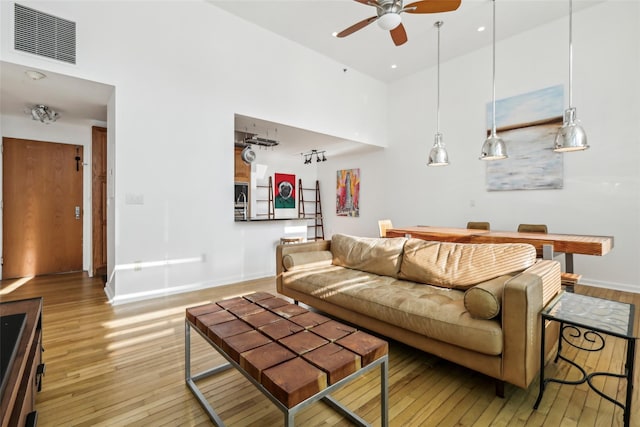 living room with ceiling fan, a towering ceiling, and light wood-type flooring