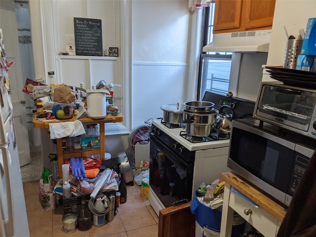 kitchen with light tile patterned floors, tile walls, and white gas stove