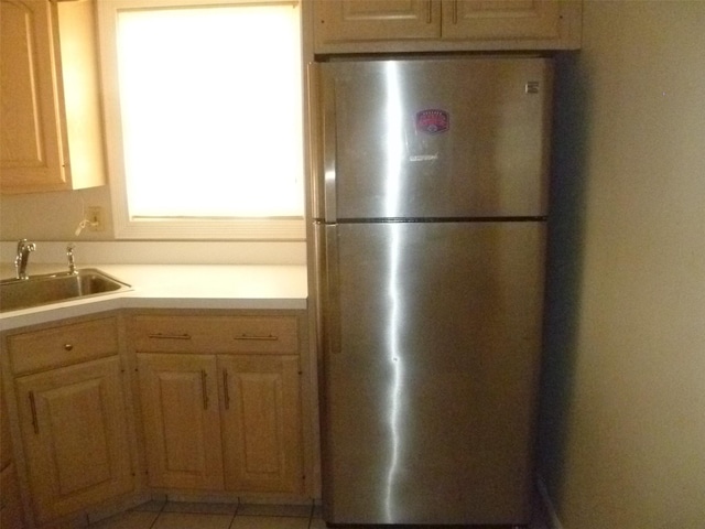 kitchen with stainless steel refrigerator, sink, light tile patterned flooring, and light brown cabinetry