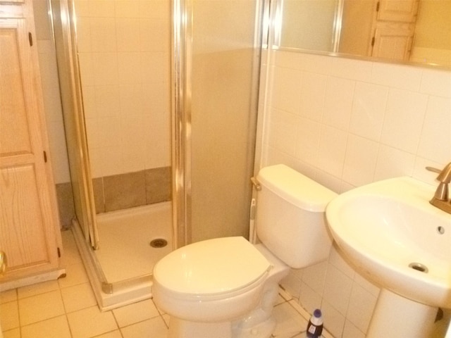 bathroom with sink, backsplash, toilet, a shower with shower door, and tile walls