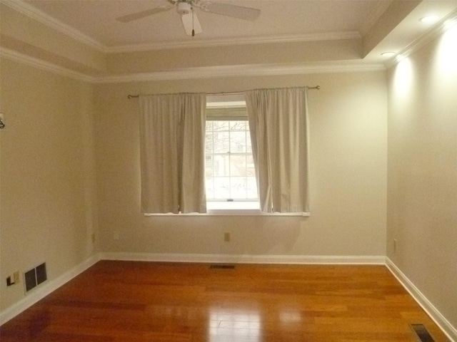 empty room featuring a tray ceiling, wood-type flooring, ornamental molding, and ceiling fan