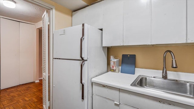 kitchen featuring white refrigerator, dark parquet flooring, white cabinetry, and sink