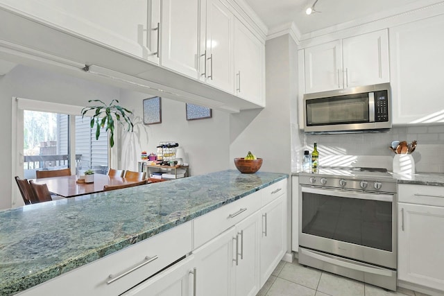 kitchen featuring stone countertops, light tile patterned floors, appliances with stainless steel finishes, decorative backsplash, and white cabinets