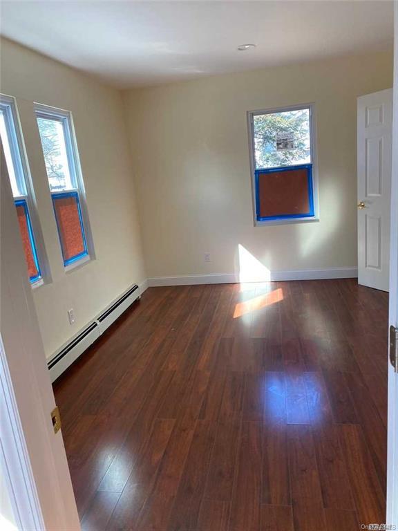 empty room with dark wood-type flooring and a baseboard heating unit