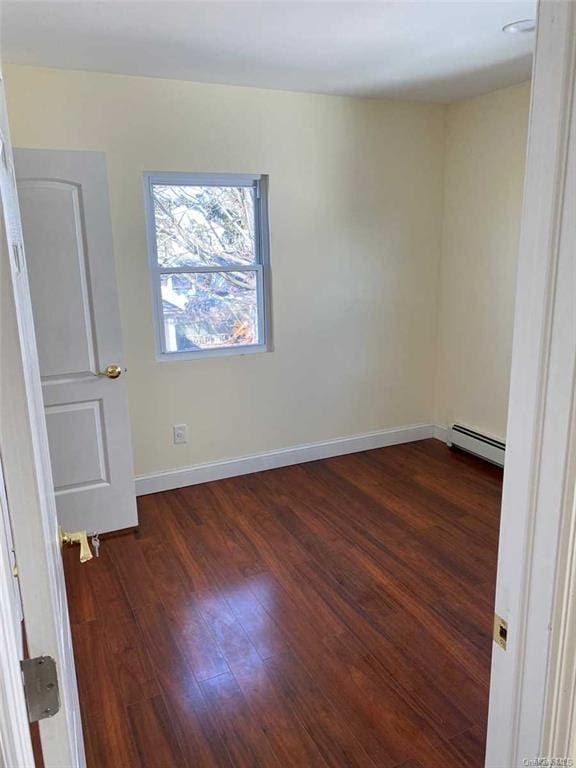 empty room featuring dark wood-type flooring and a baseboard heating unit