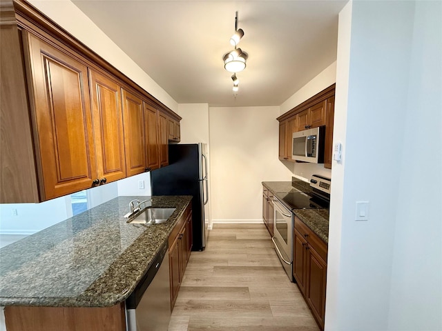 kitchen featuring sink, kitchen peninsula, dark stone countertops, light hardwood / wood-style floors, and appliances with stainless steel finishes