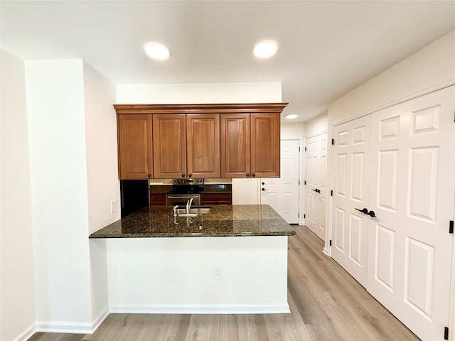 kitchen featuring kitchen peninsula, light wood-type flooring, sink, and dark stone countertops