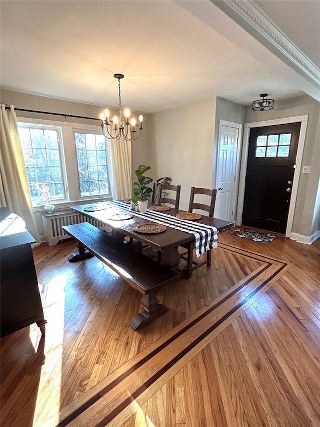 dining area featuring radiator heating unit, hardwood / wood-style floors, ornamental molding, and an inviting chandelier