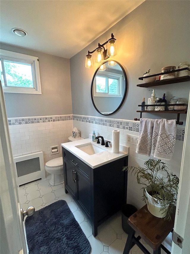 bathroom with tile patterned flooring, heating unit, toilet, vanity, and tile walls