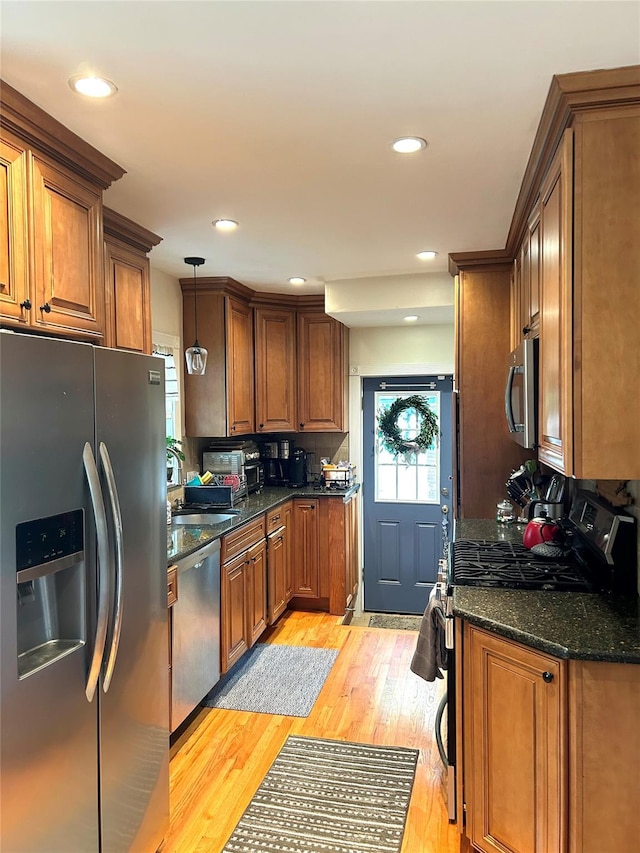 kitchen with pendant lighting, dark stone countertops, appliances with stainless steel finishes, and light hardwood / wood-style flooring