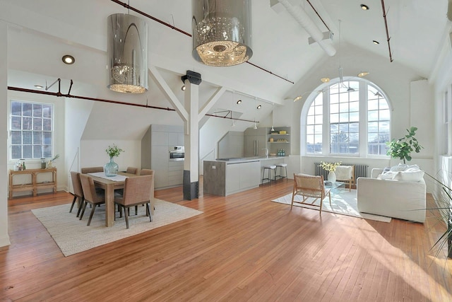 dining area with high vaulted ceiling and light hardwood / wood-style flooring