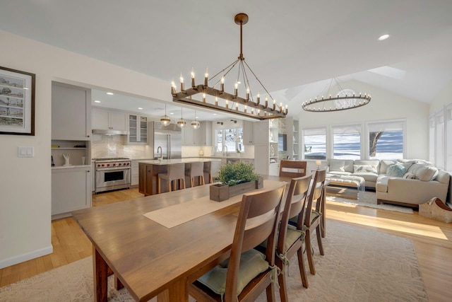 dining space featuring a notable chandelier, light hardwood / wood-style flooring, sink, and vaulted ceiling