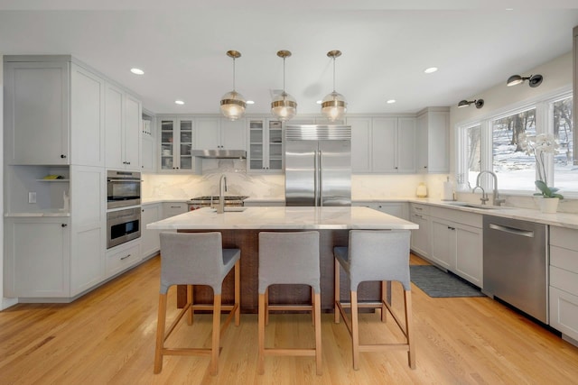 kitchen with pendant lighting, appliances with stainless steel finishes, sink, and an island with sink