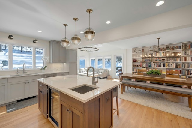 kitchen featuring wine cooler, sink, light stone counters, and a center island with sink