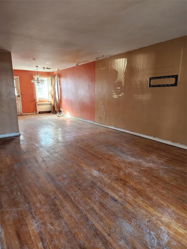 spare room with radiator, wood-type flooring, and a notable chandelier