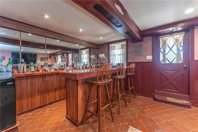 bar featuring beam ceiling, hanging light fixtures, and wooden walls