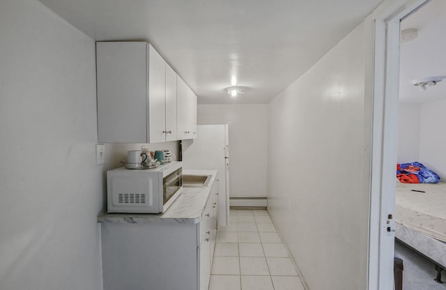 kitchen with white cabinets, light tile patterned floors, and baseboard heating