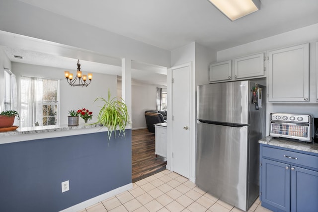 kitchen with hanging light fixtures, light tile patterned floors, stainless steel fridge, white cabinetry, and an inviting chandelier