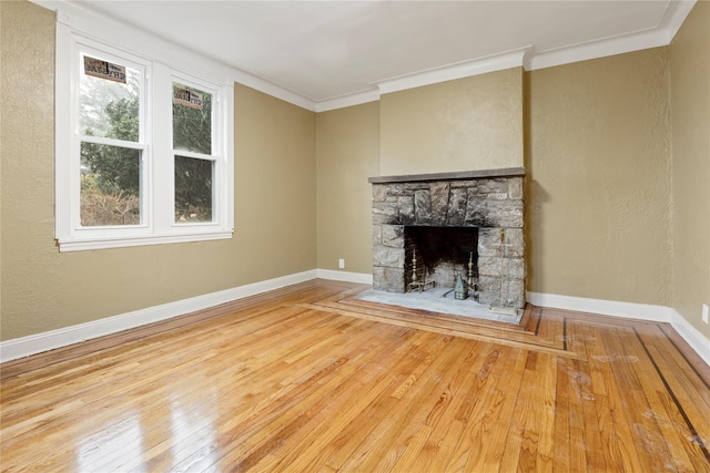 unfurnished living room with hardwood / wood-style flooring, a stone fireplace, and ornamental molding